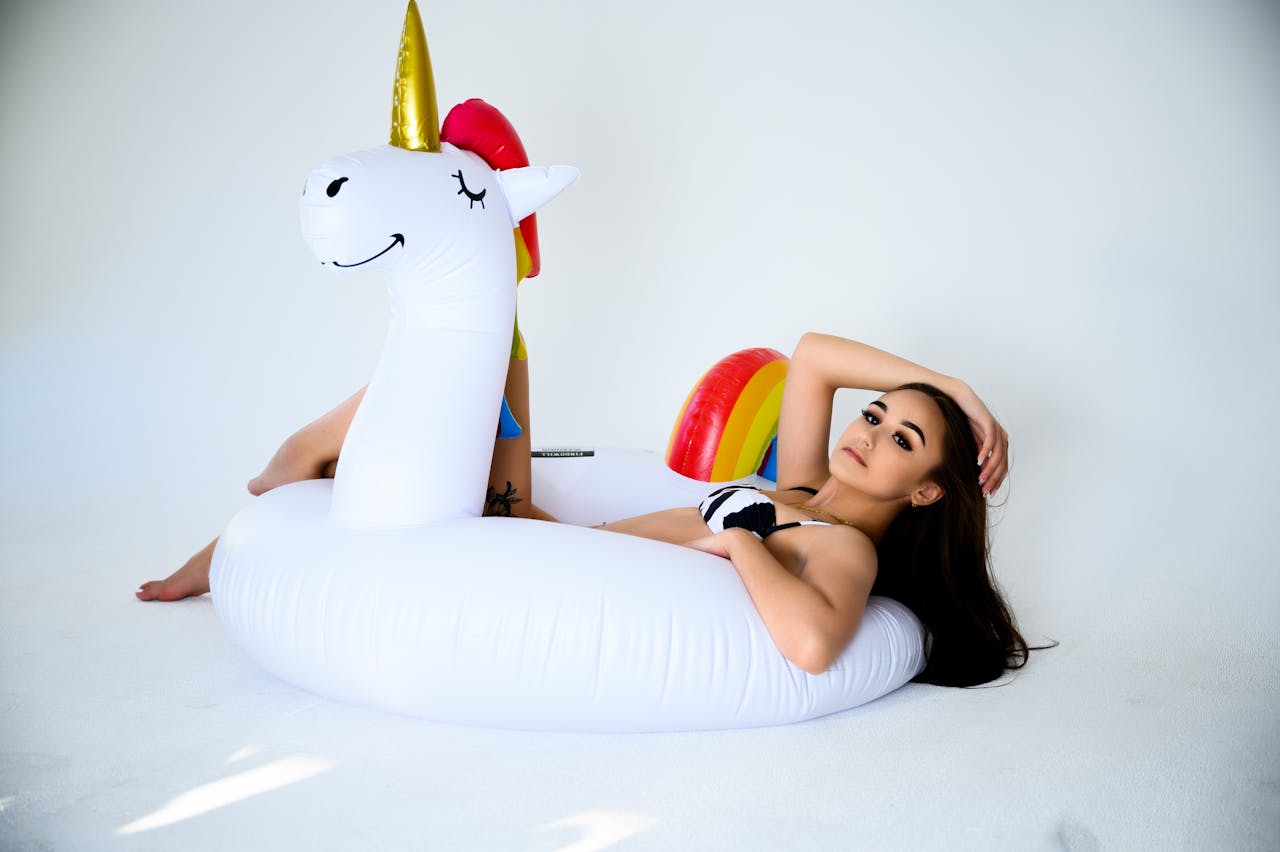 hero-img-02 A young woman lounging on a unicorn float during a studio photoshoot, exuding a summer vibe.